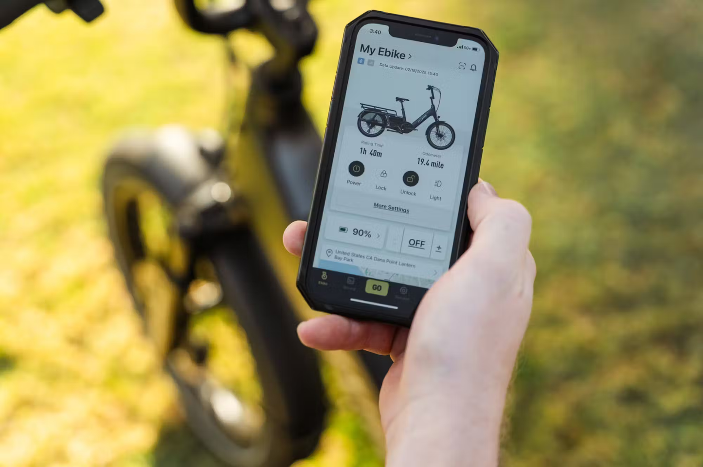 Hand holding smartphone displaying app connected to Aventon Abound LR cargo e-bike by Rex E-Bikes
