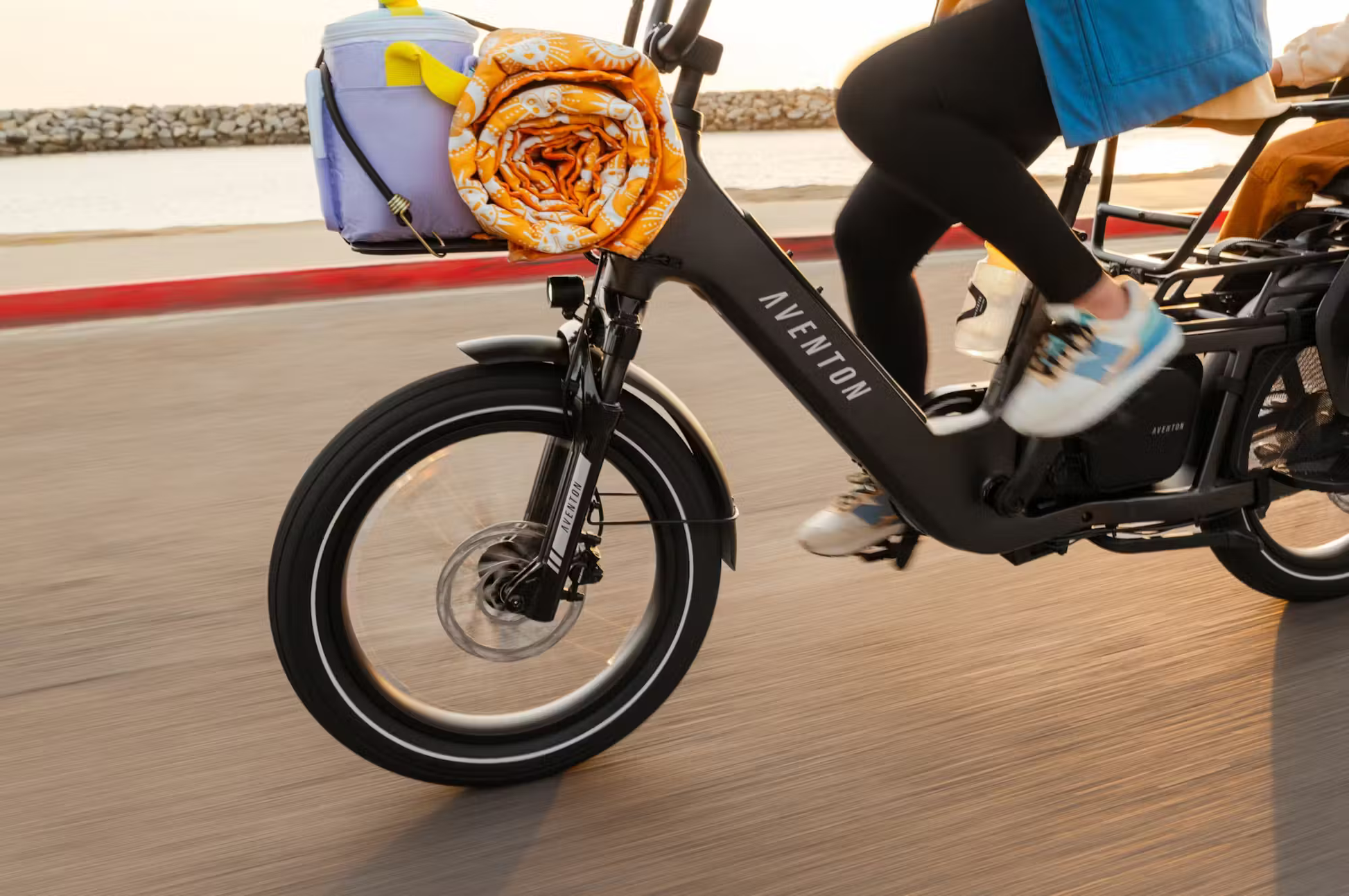 Rex E-Bikes Aventon Abound LR cargo e-bike in motion with front cargo carrying picnic supplies