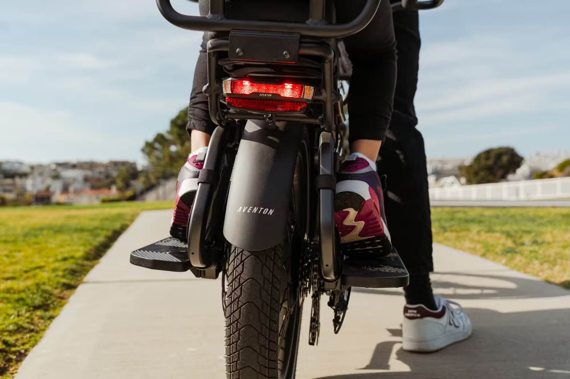 Rear view of Aventon Abound LR cargo e-bike showing large rear tire and footrests on a sunny path