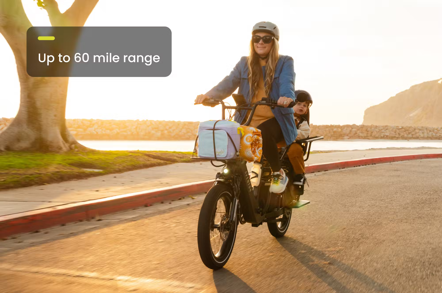 Rex E-Bikes Aventon Abound LR cargo e-bike with a woman and child riding on a road at sunset