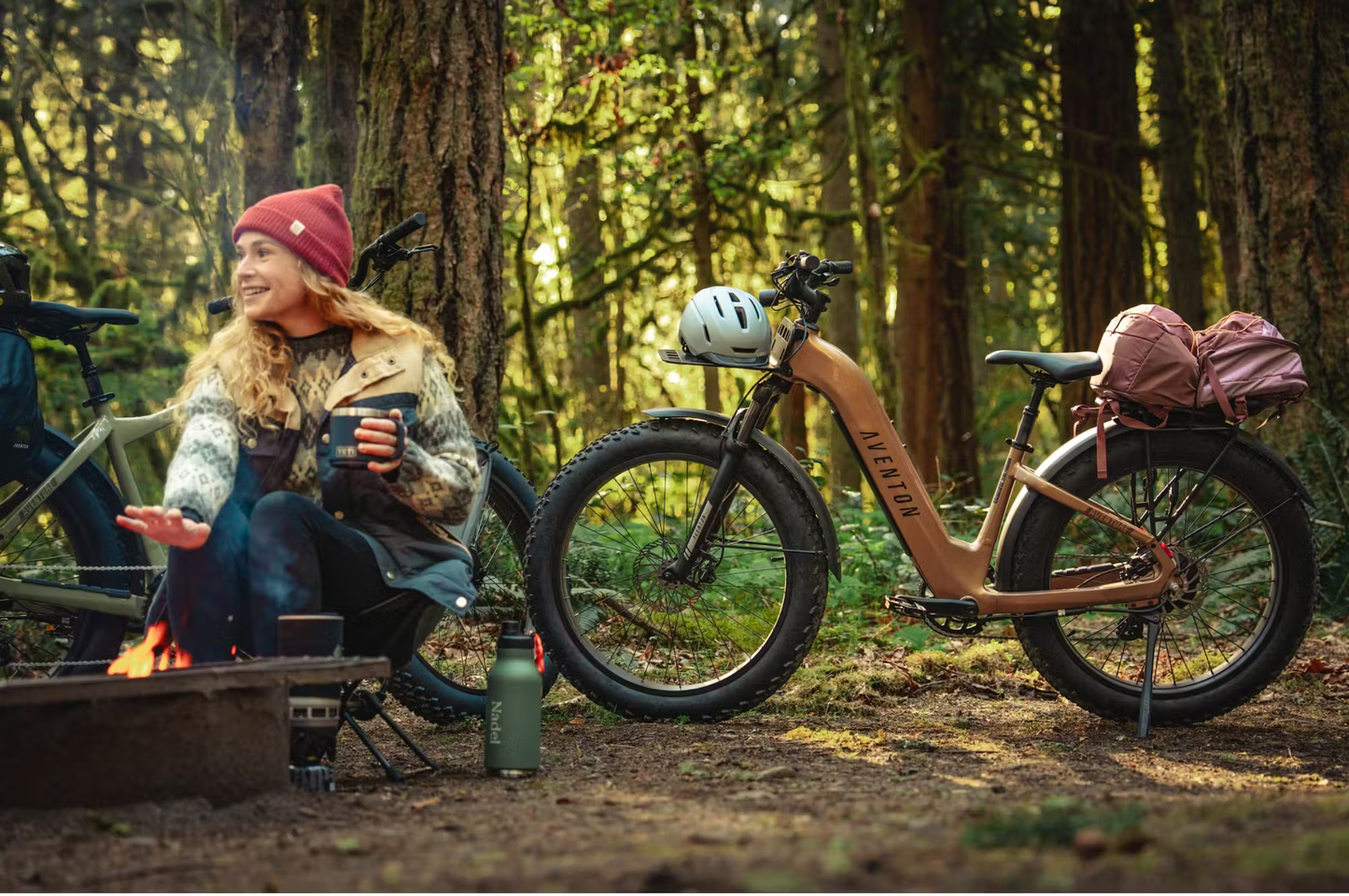 Rex E-Bikes Aventon Aventure.3 step-through e-bike parked in forest campsite with gear and helmet