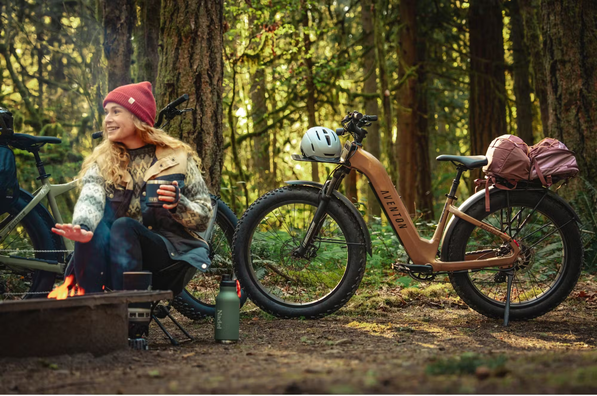 Rex E-Bikes Aventon Aventure.3 step-through e-bike parked in forest campsite with gear and helmet