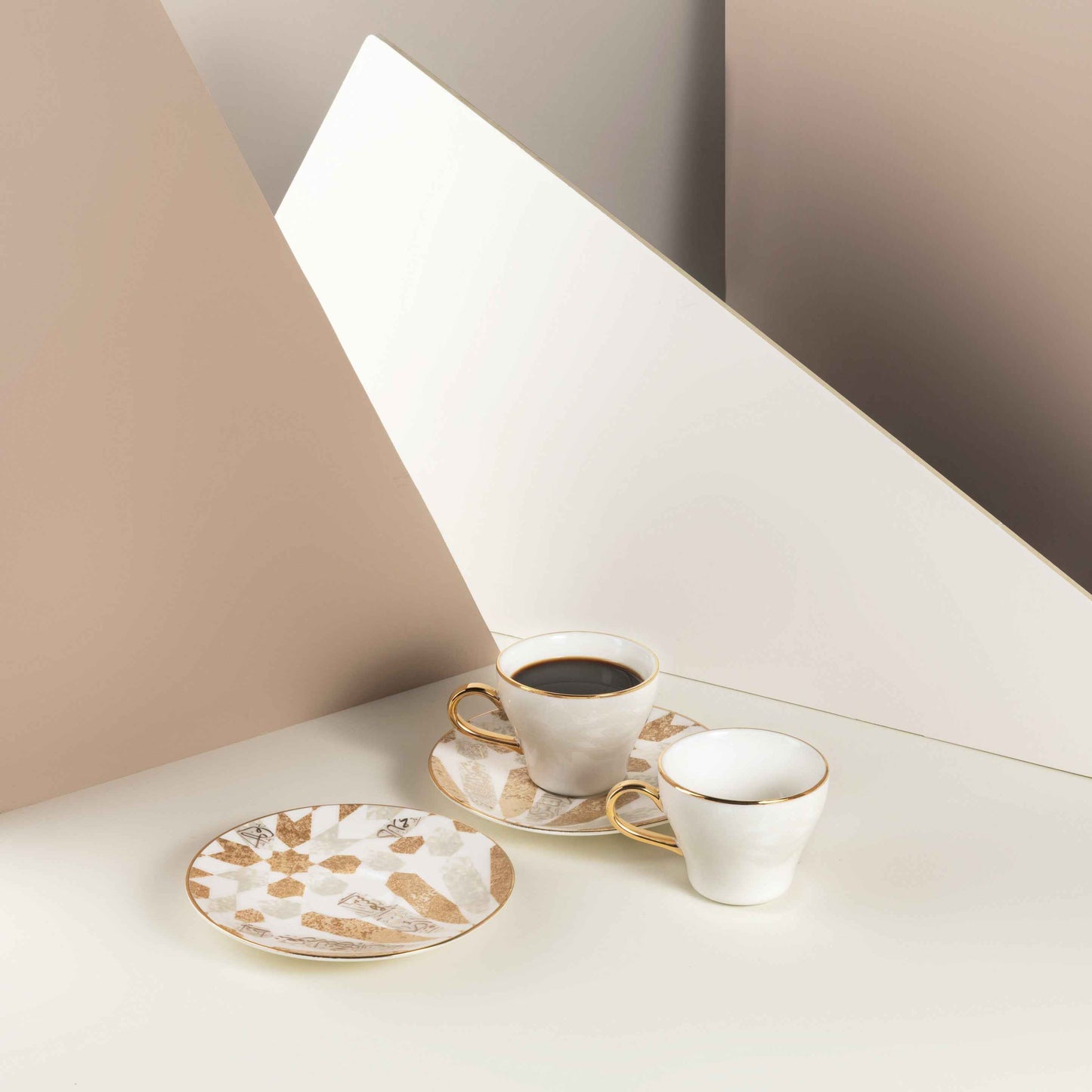 Beige and gold espresso cups set with matching saucers displayed on a cream surface