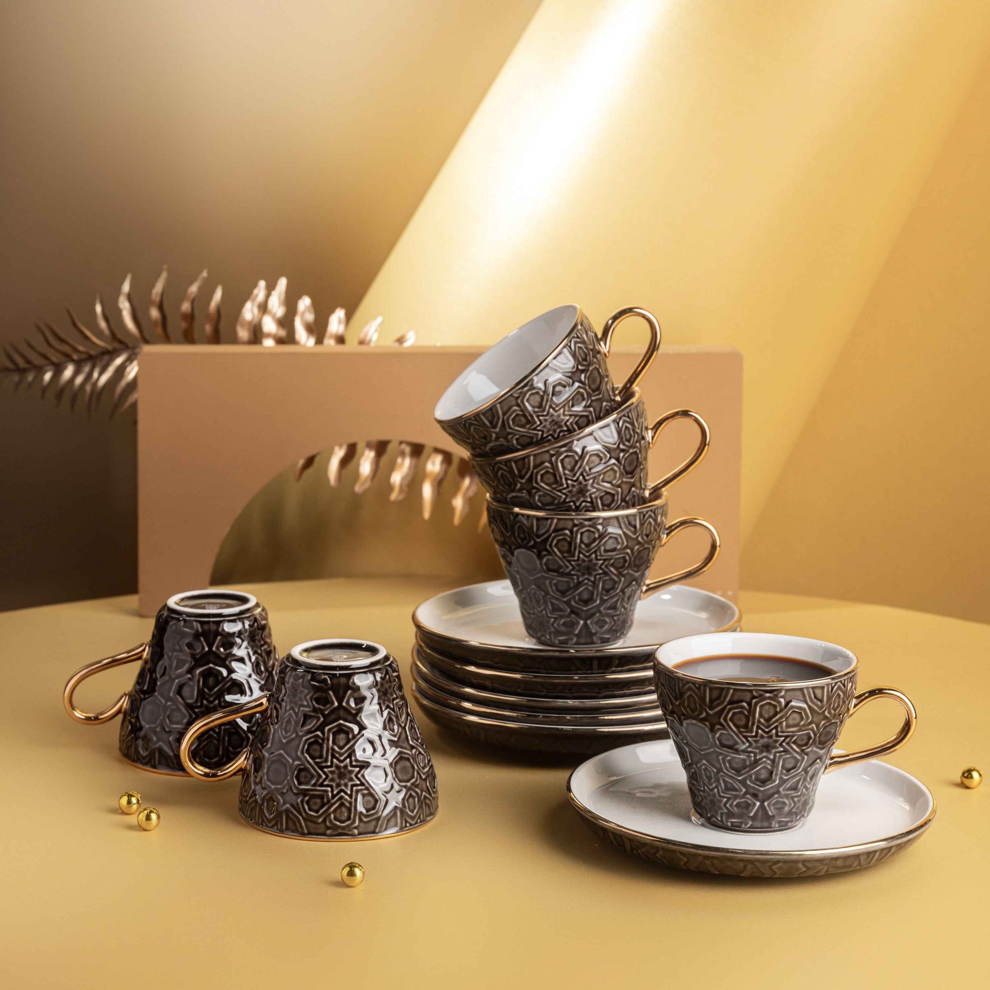 Otantik Home black and gold espresso cup set with intricate patterns and matching saucers stacked on a beige surface
