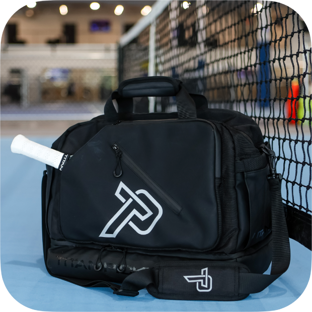 Black Titan duffle bag pickleball bag with white logo and racket handle pocket on blue court