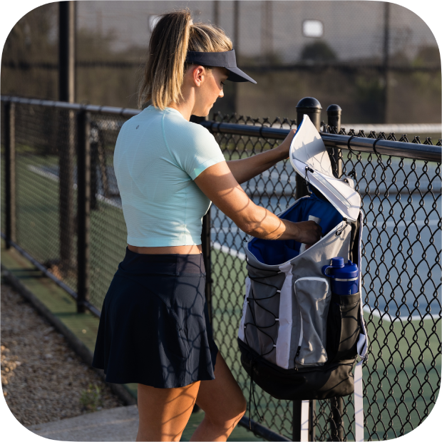 Woman opening a Titan Pickleball Backpack by a tennis court fence with water bottle holder