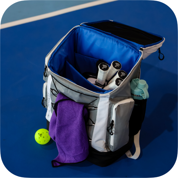Open Titan Pickleball Backpack with blue interior holding pickleball paddles, towel, and water bottle on court