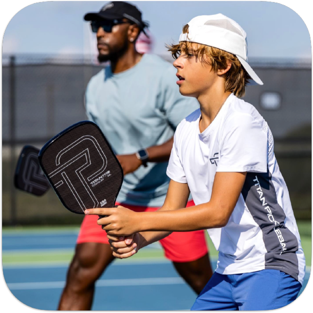 Young player wearing a white Titan pickleball hat while playing pickleball outdoors with a partner