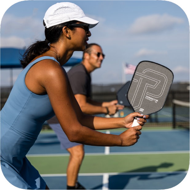 Woman holding Titan Pro Titanium pickleball paddle playing pickleball on outdoor court with male player