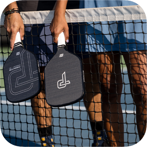 Two players holding Titan Pro Titanium pickleball paddles over the net on an outdoor court