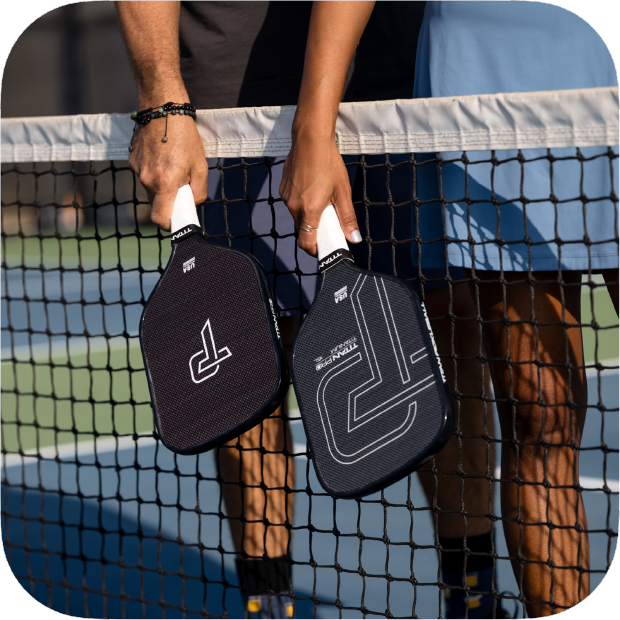 Two players holding Titan Pro Titanium pickleball paddles over the net on an outdoor court